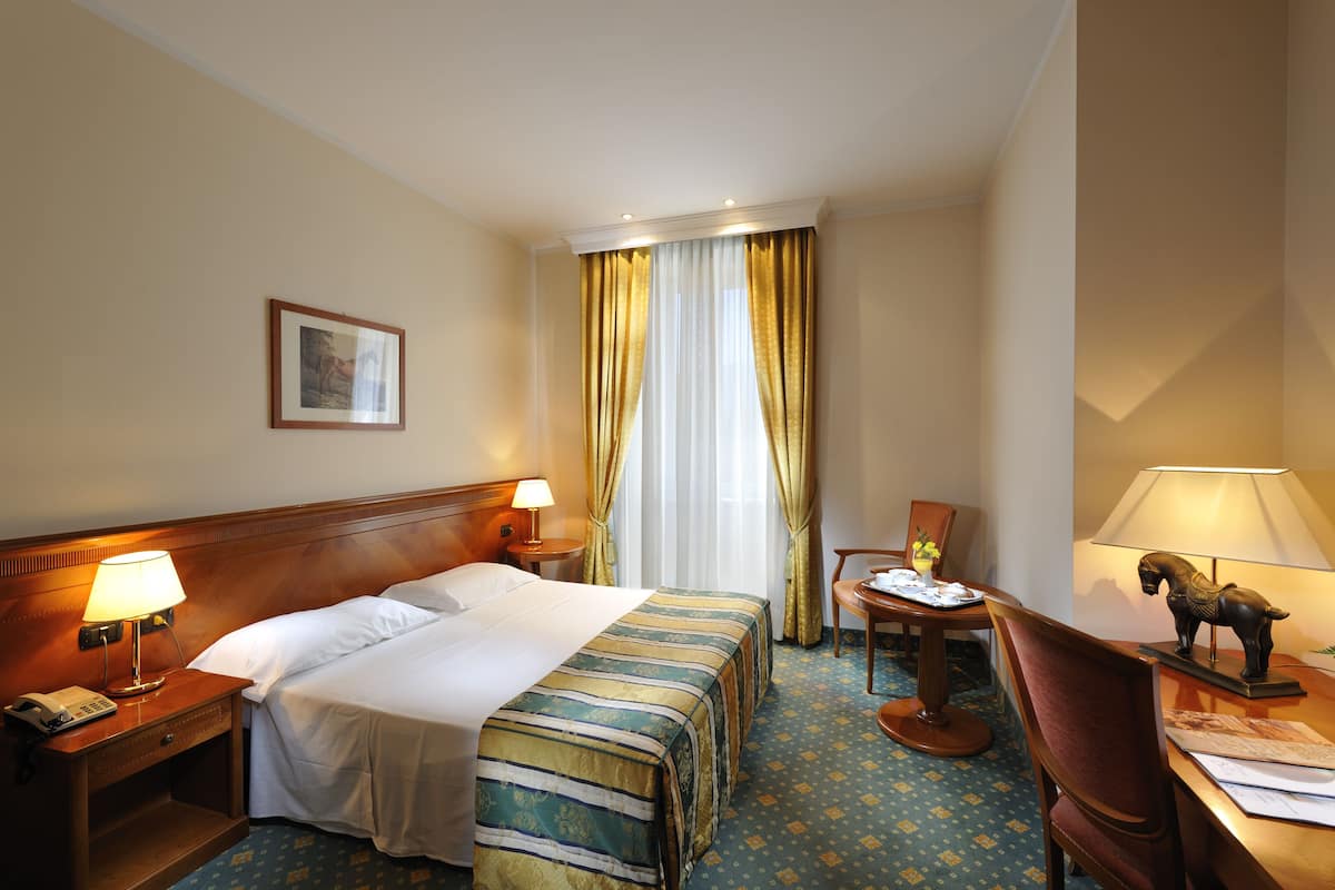 Ein Hotelzimmer mit einem Bett, zwei Nachttischen mit Lampen, einem Sessel, einem Schreibtisch mit Lampe und einer kleinen dekorativen Pferdestatue.