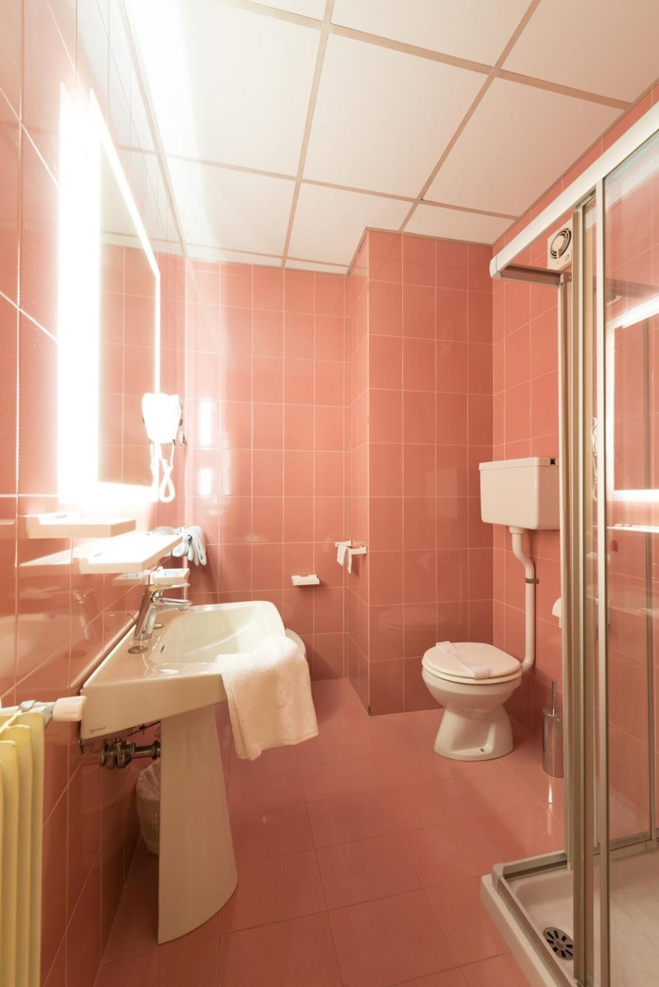 A bathroom with pink tiles, a sink, a toilet, and a shower area.
