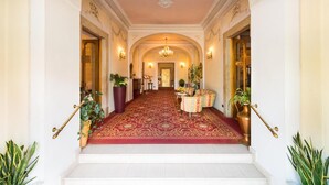 A grand hallway with a red carpet, ornate columns, and a chandelier. - Hotel Eden Levico Terme (Levico Terme)