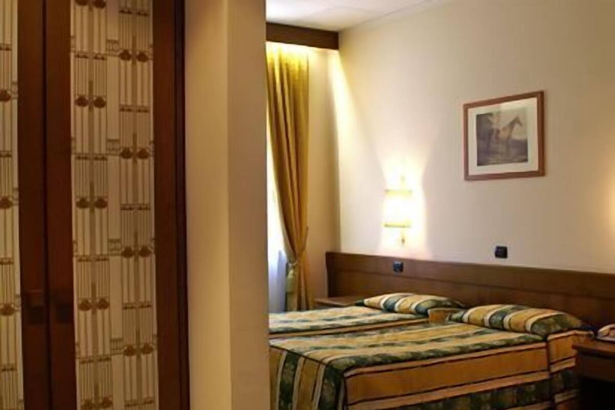 Ein Hotelzimmer mit einem Bett, einem Nachttisch, einer Lampe und einem gerahmten Bild an der Wand.