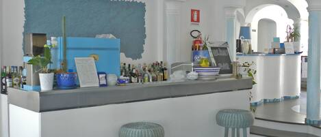 Zona de bar con taburetes, una barra con diversas botellas, una pared decorativa azul y un letrero que dice "Holiday Bar".