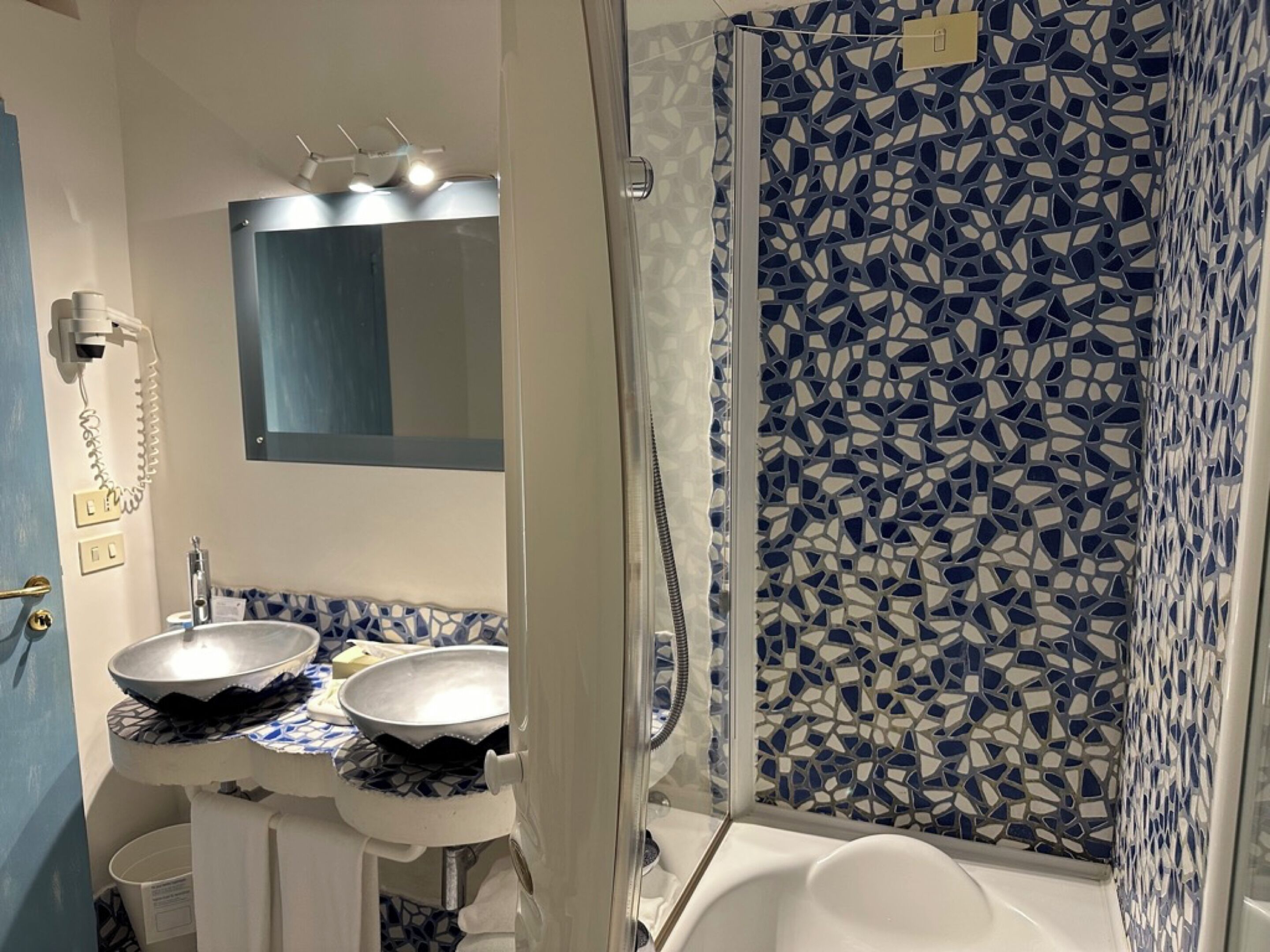 Un baño con dos lavamanos, un espejo y una ducha con mosaicos.