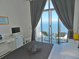 Habitación de hotel con cama, escritorio con computadora, silla y vista al mar.