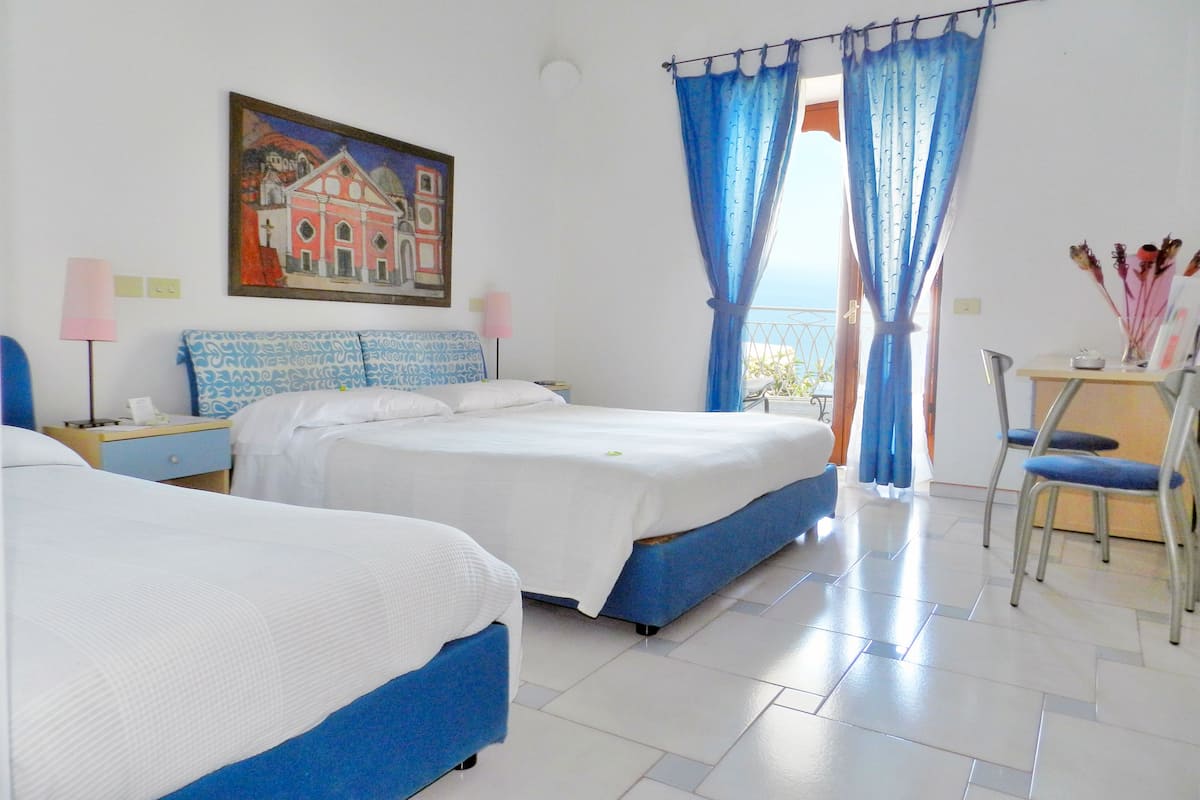 A hotel room with two beds, a painting on the wall, and a balcony with blue curtains.
