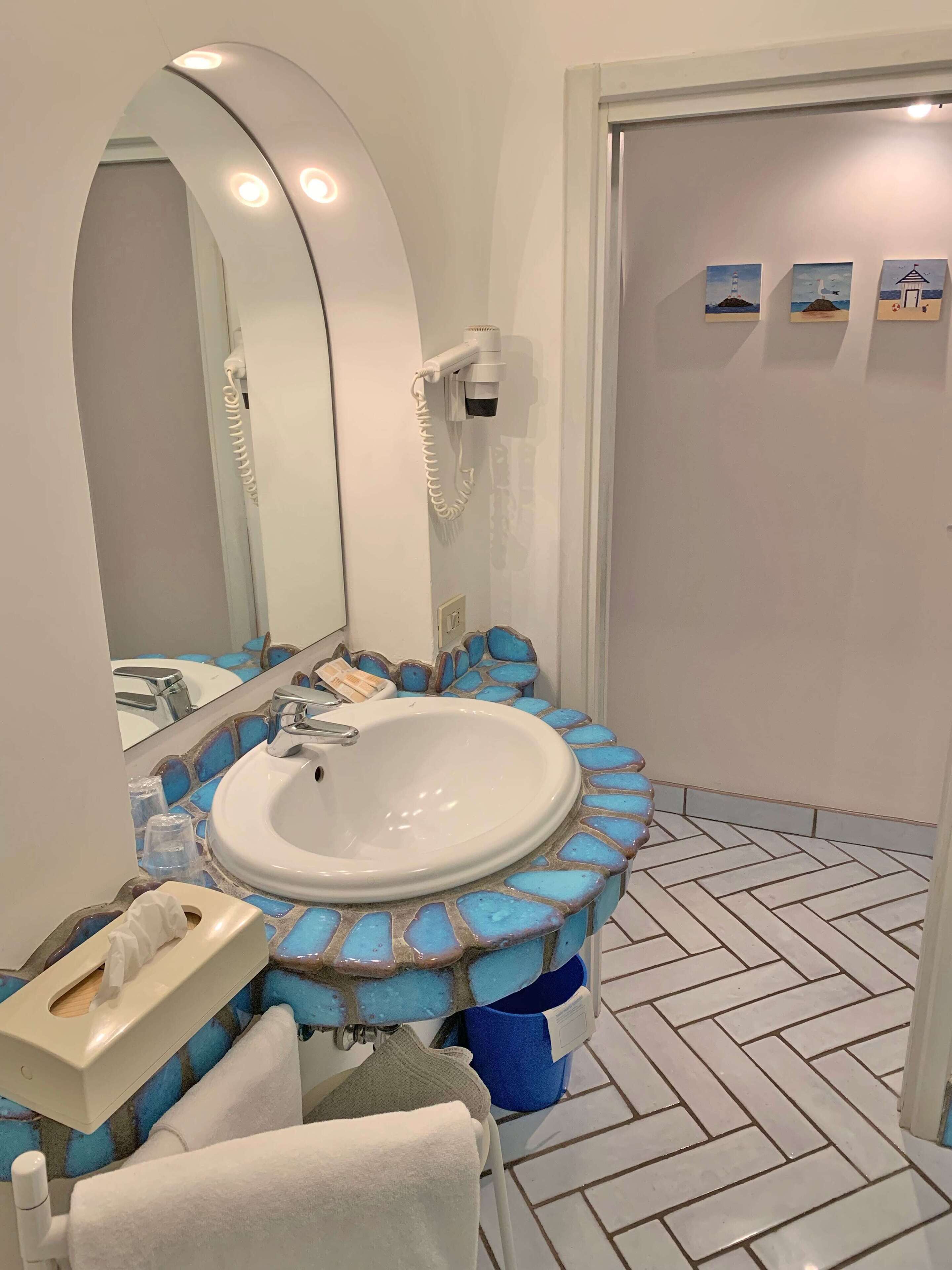 A bathroom with a white sink, a mirror, and a hairdryer mounted on the wall.