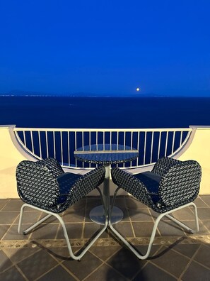 Un balcón con dos sillas y una mesa, con vista a una masa de agua de noche.