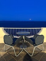 Un balcón con dos sillas y una mesa, con vista a una masa de agua de noche.