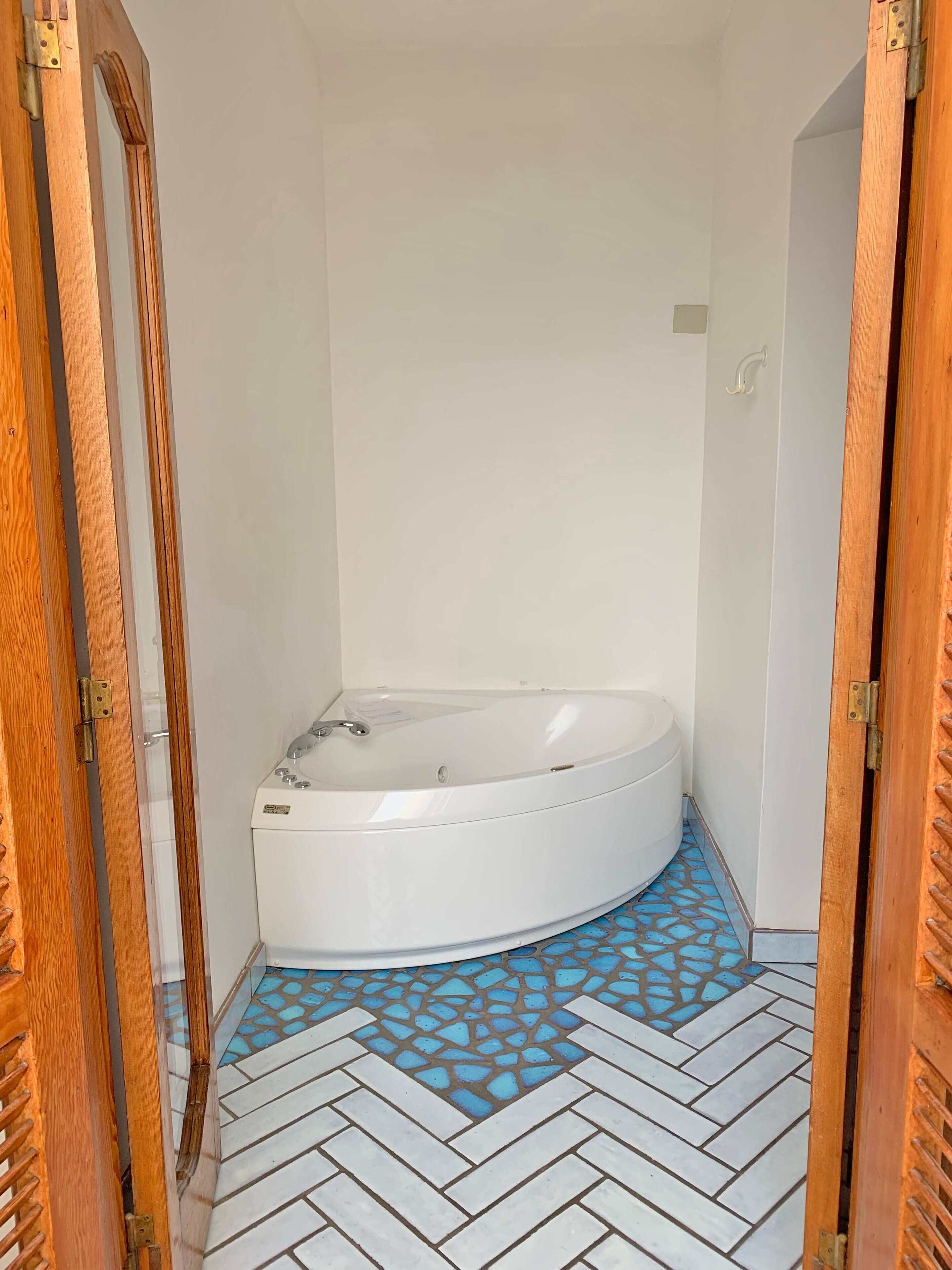 Un baño pequeño y cerrado con una bañera blanca, piso de baldosas con diseño azul y puertas de madera.