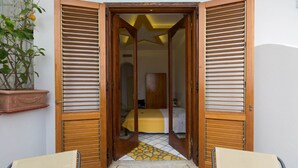 Una puerta con contraventanas de madera que da a una habitación con una cama y una colcha amarilla.