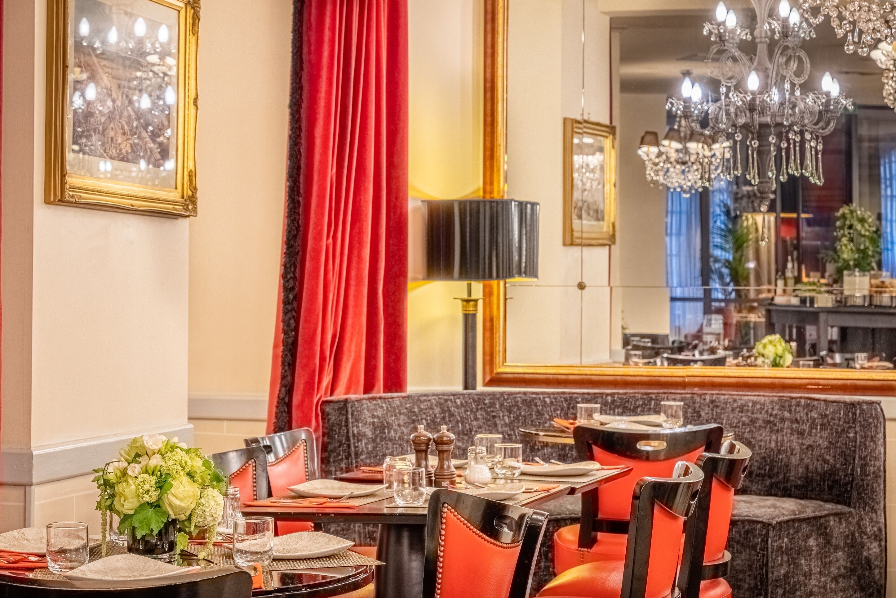 A dining area with a chandelier, red curtains, and a mirror reflecting the room.