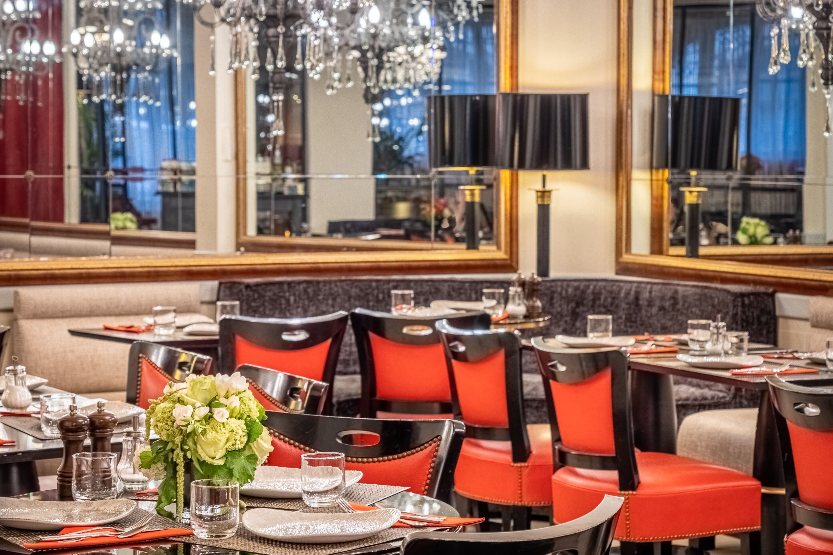A restaurant interior with round tables, red and black chairs, and a chandelier.