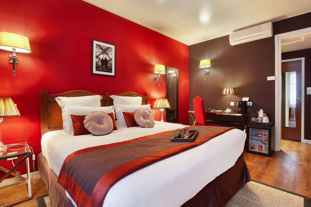 Ein Hotelzimmer mit einem großen Bett, roten Wänden und einem Schreibtisch mit einem Computer.