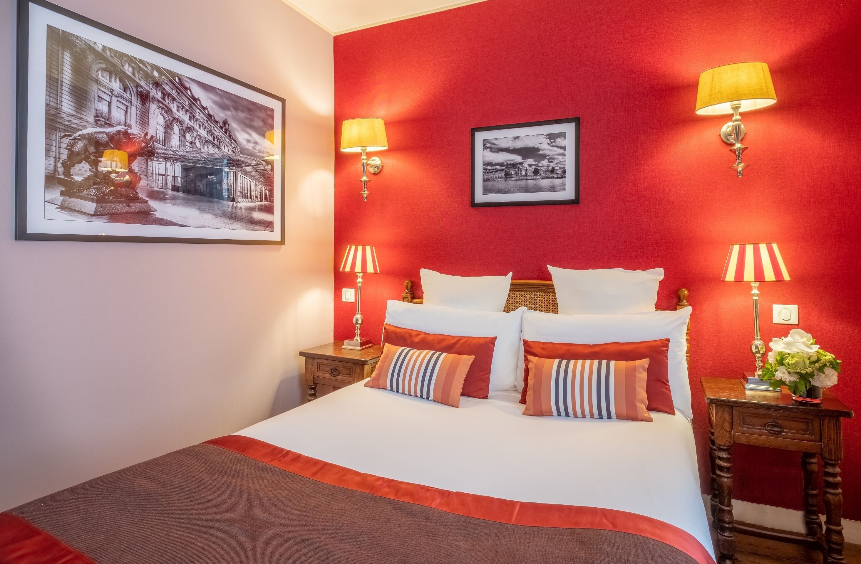 A hotel room with a large bed, red walls, and two bedside tables with lamps.