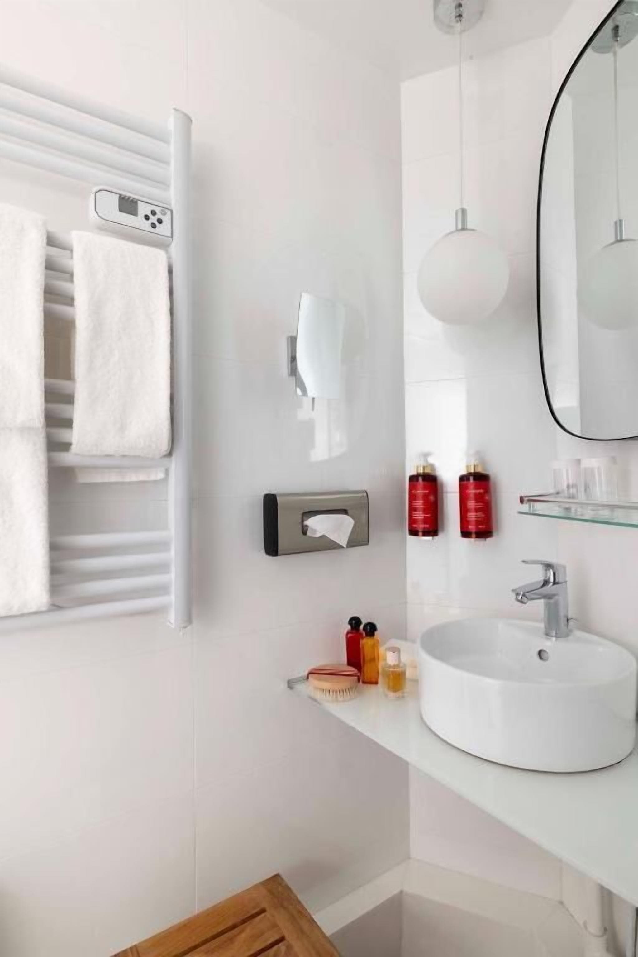 A modern bathroom with a white sink, a towel rack with white towels, a handheld showerhead, and a mirror.