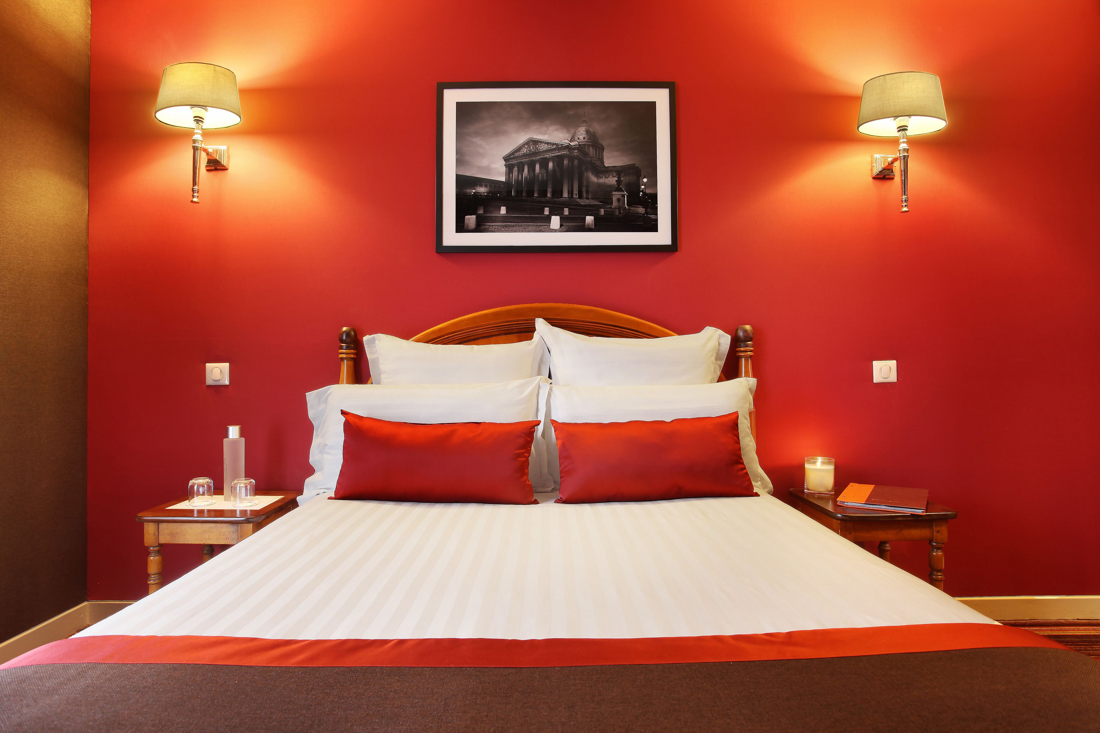 Une chambre d’hôtel avec un grand lit, des murs rouges et deux lampes fixées au mur.