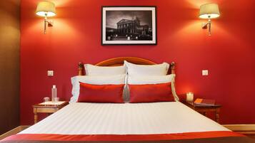 Une chambre d’hôtel avec un grand lit, des murs rouges et deux lampes fixées au mur.