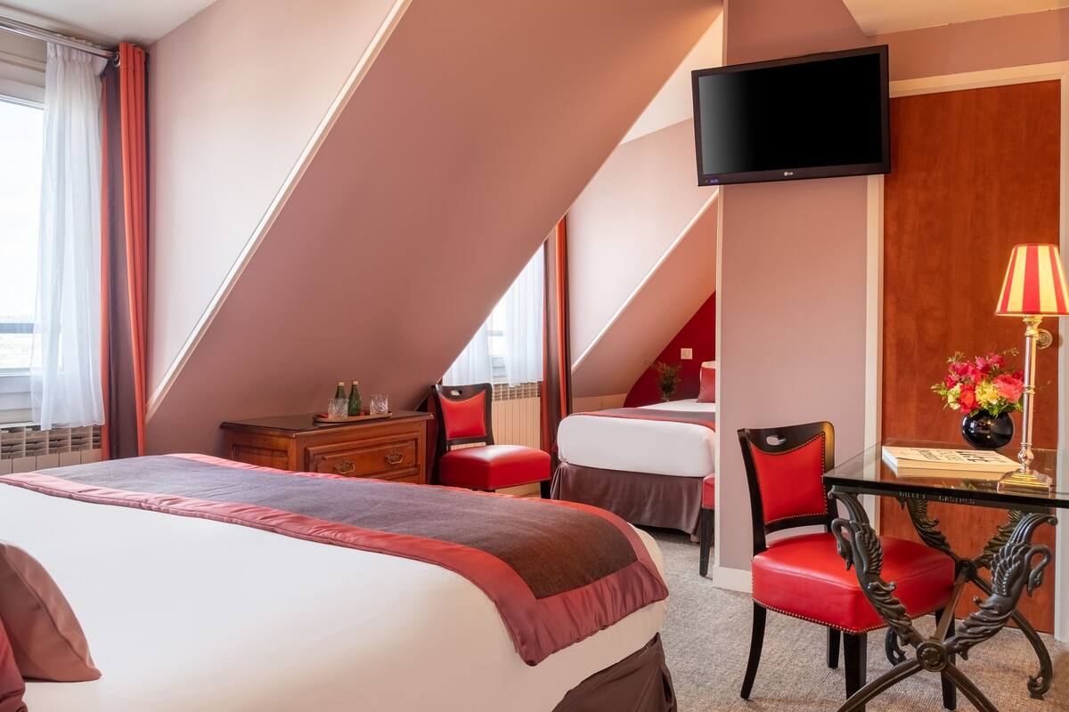 Ein Hotelzimmer mit einem großen Bett, einem Schreibtisch mit Lampe, einem Fernseher und einem Fenster mit Vorhängen.