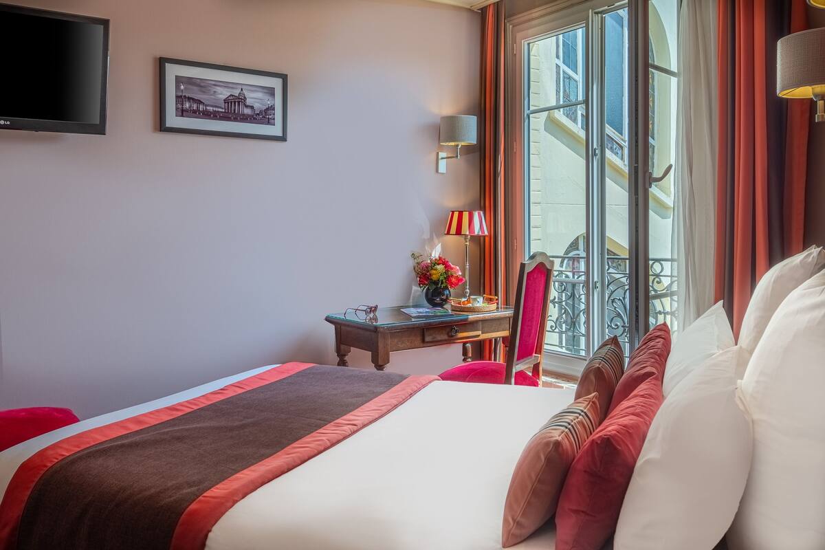 Ein Hotelzimmer mit Bett, Schreibtisch, Stuhl, Fernseher und einem Fenster mit Vorhängen.