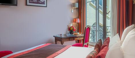 Habitación de hotel con cama, escritorio, silla, televisor y ventana con cortinas.