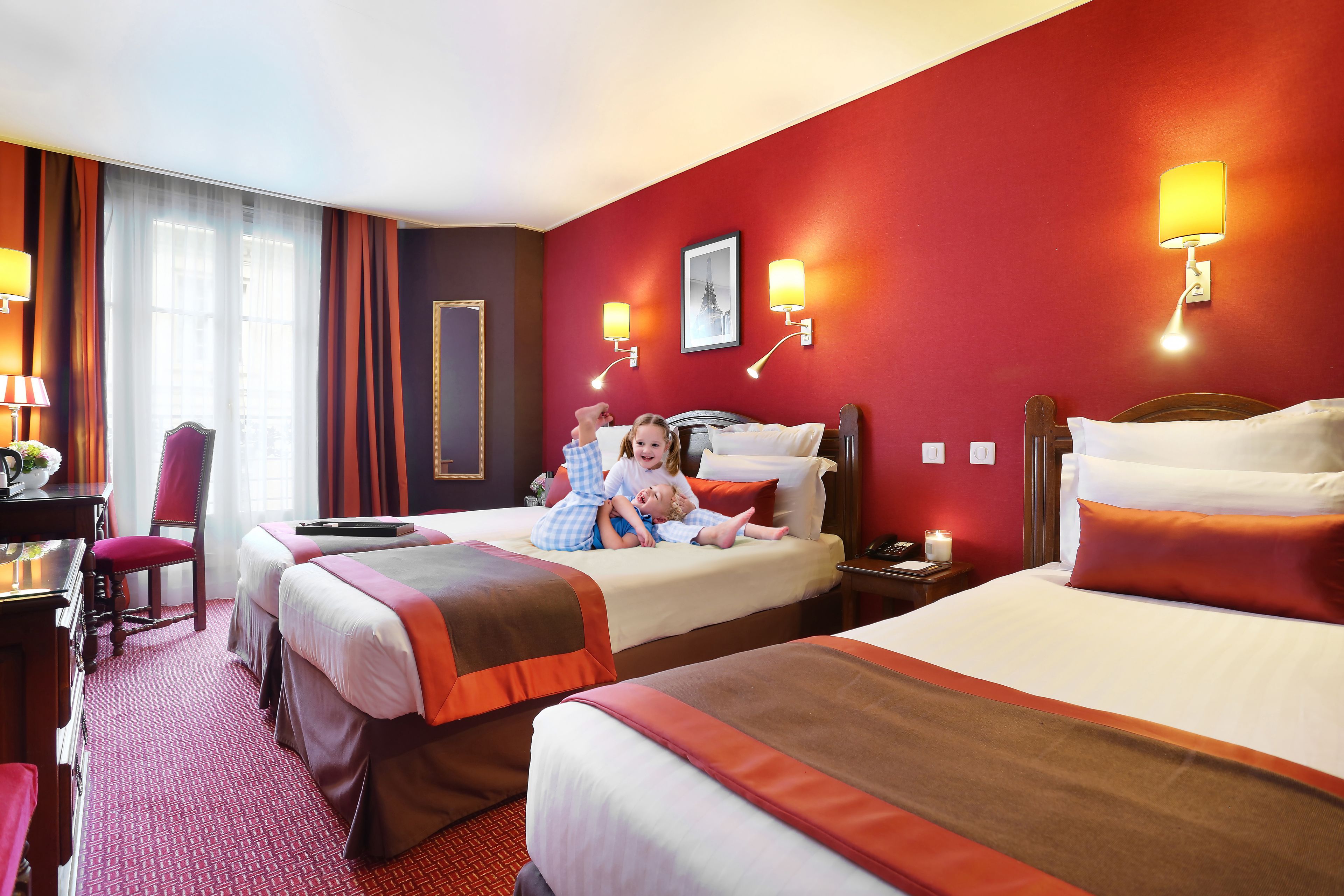 A hotel room with two beds, a desk, a chair, and a lamp.