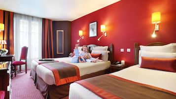 A hotel room with two beds, a desk, a chair, and a lamp.
