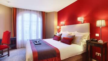 A hotel room with a large bed, red walls, and a window with curtains.