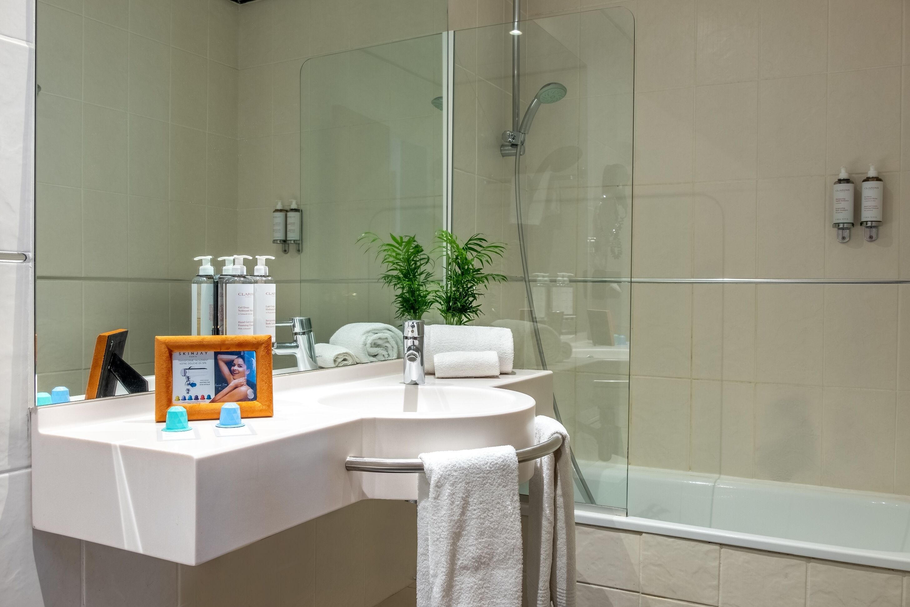 Un baño moderno con cabina de ducha de vidrio, un lavabo blanco con espejo y una pequeña planta en maceta.