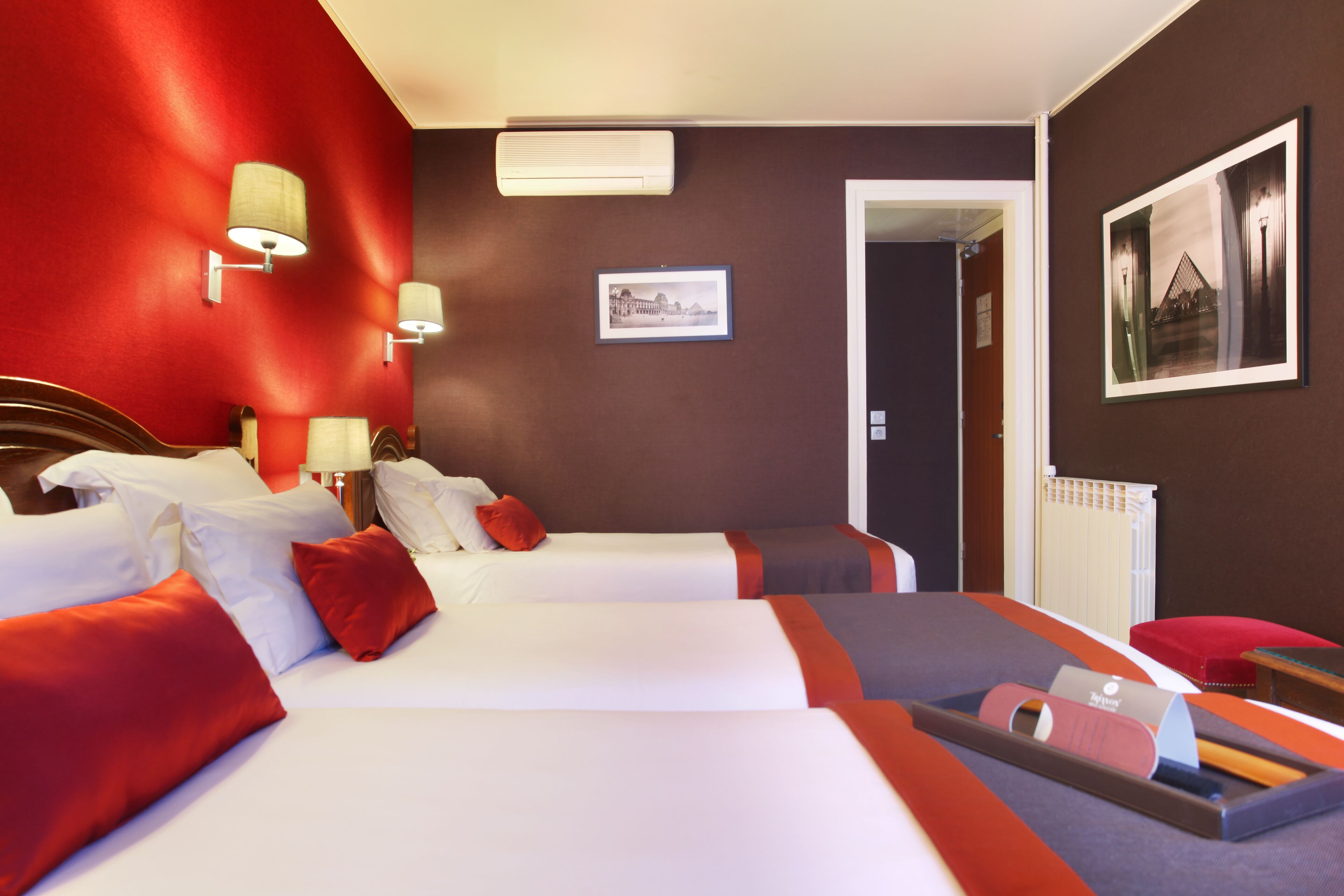 A hotel room with two beds, a red accent wall, a framed picture, and a radiator.