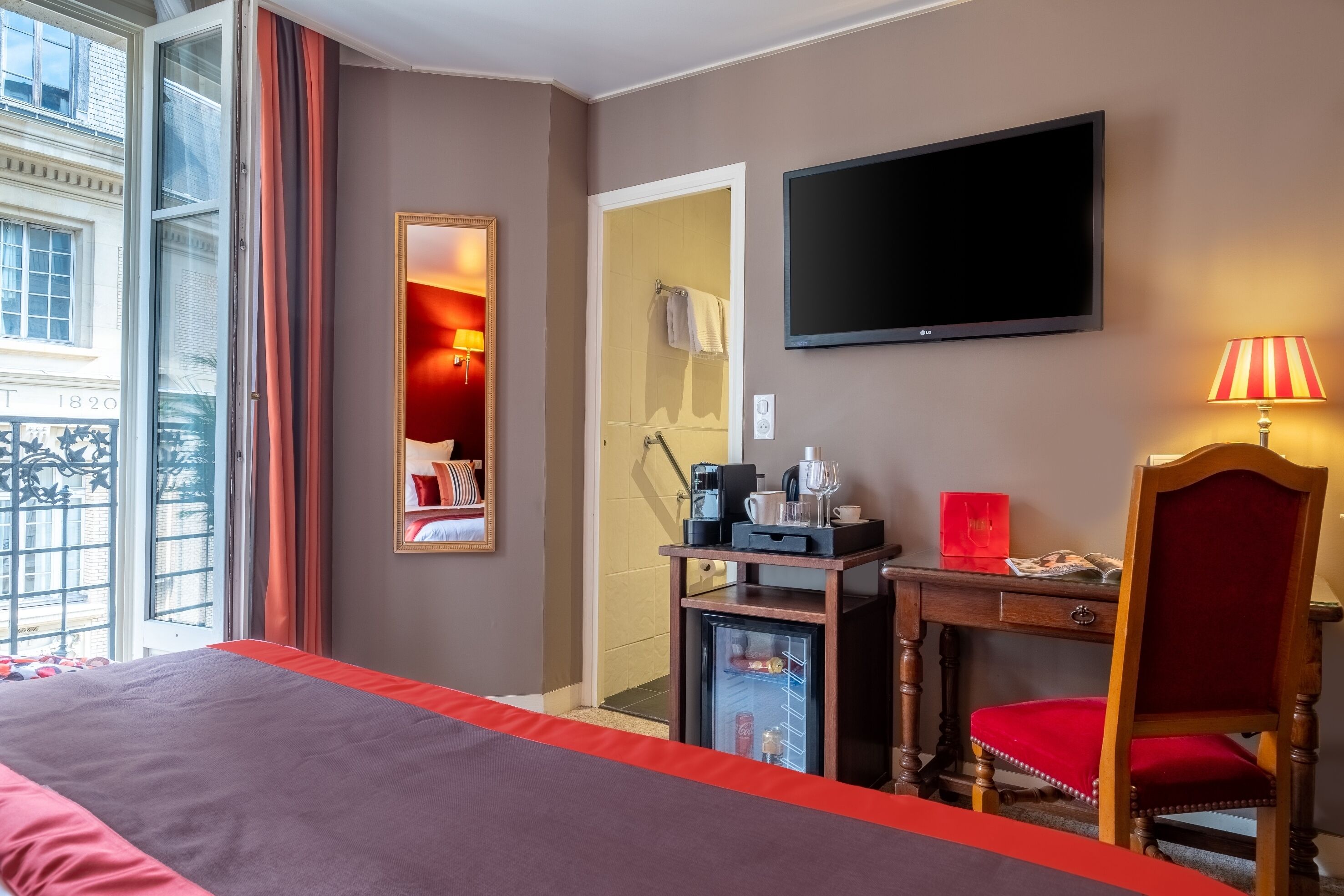 A hotel room with a bed, a desk with a coffee maker, a TV, and a chair.