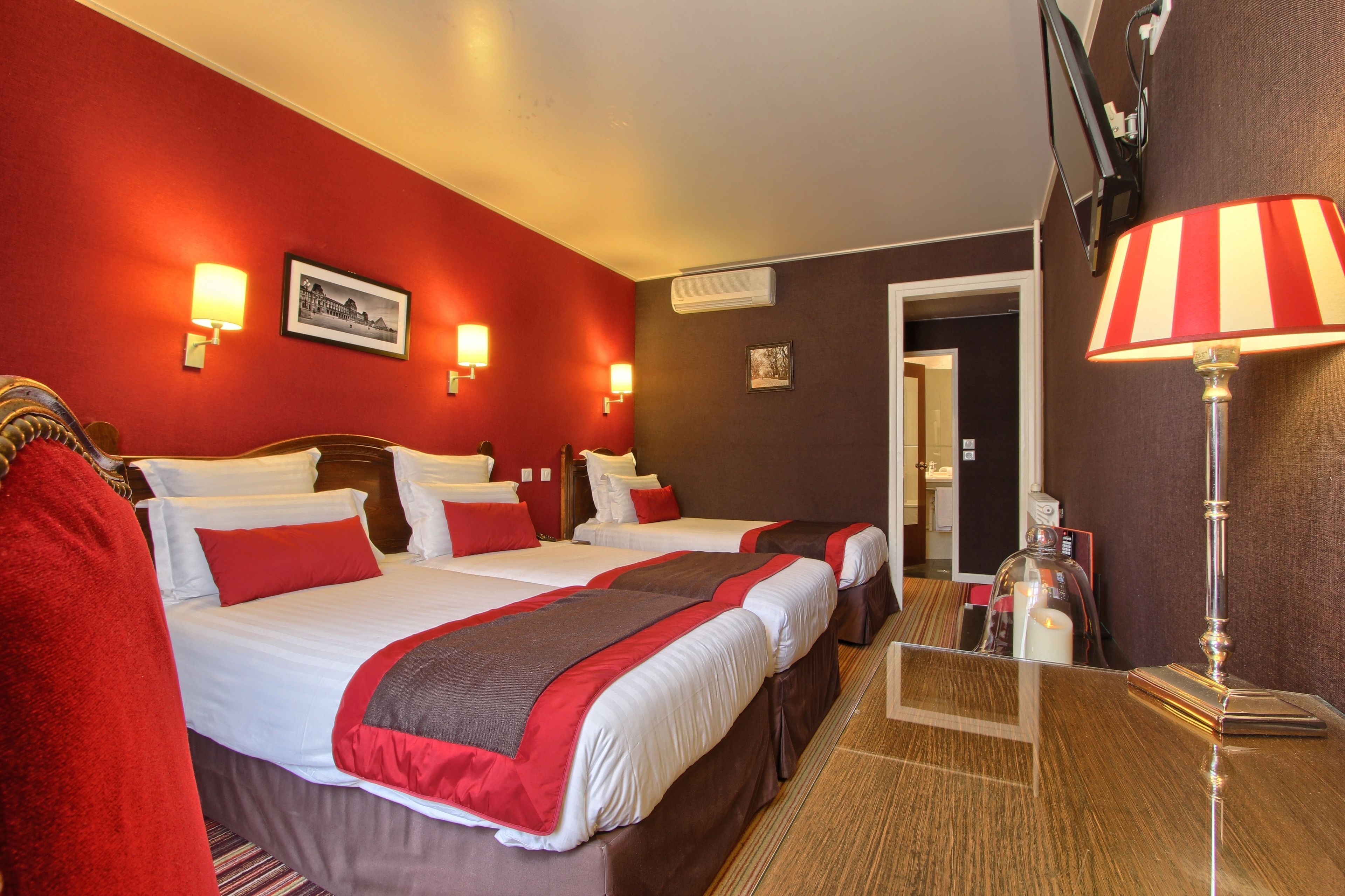 A hotel room with two beds, red and white bedding, a wooden headboard, a red and white striped lamp, and a framed picture on the wall.