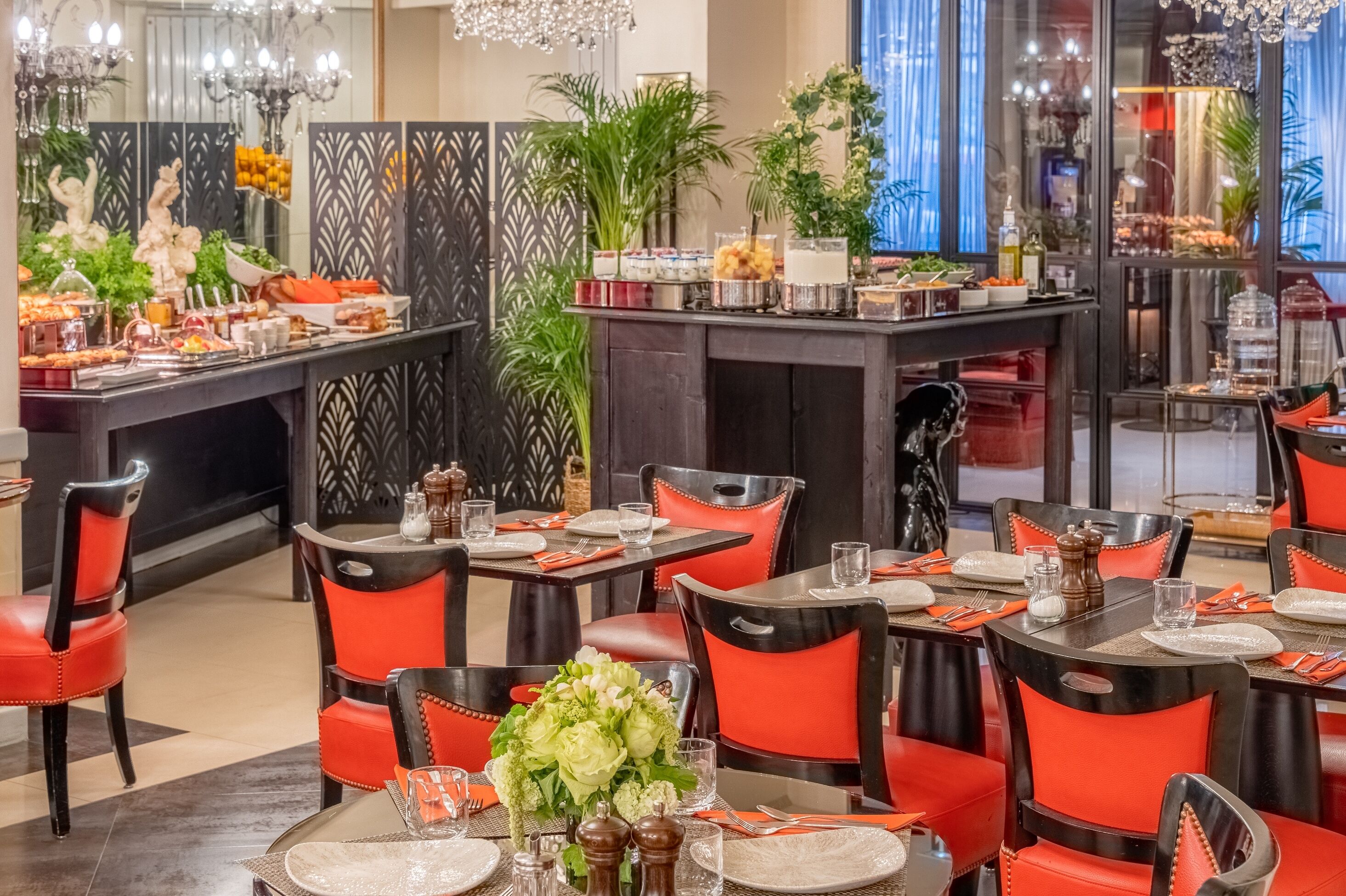 A restaurant with red and black chairs, tables set with plates, glasses, and cutlery.