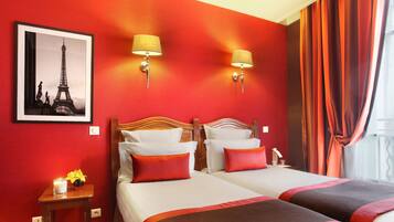 A hotel room with two beds, red walls, a framed picture of the Eiffel Tower, and two wall-mounted lamps.