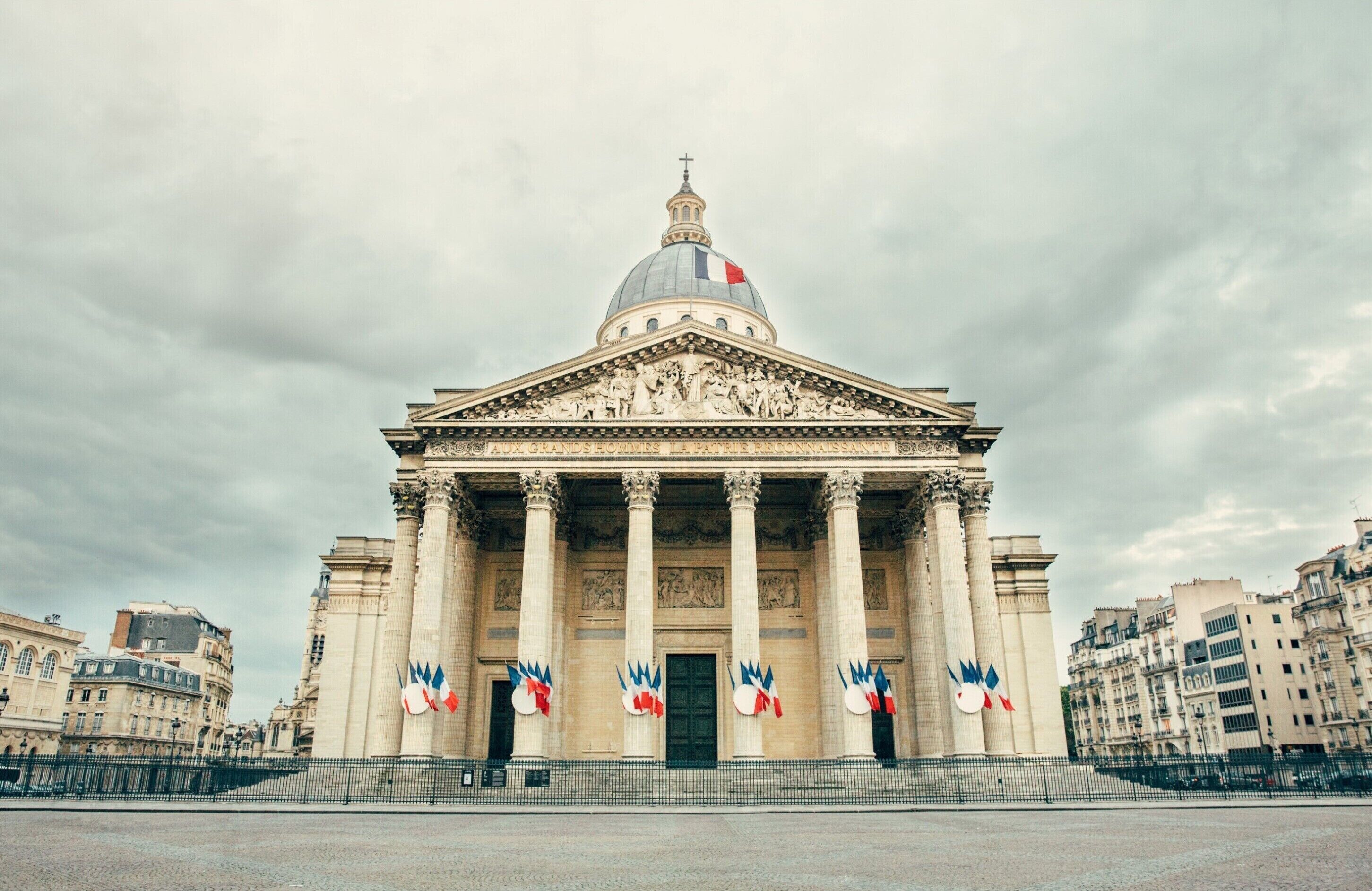A grand neoclassical building with a large dome and columns, featuring a prominent entrance and a flag display.