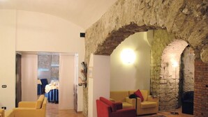 A room with a stone archway, yellow sofas, and a dining area in the background. - Caravaggio Hotel (Naples)