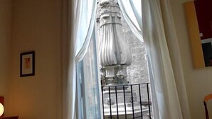 A room with a bed, a window with white curtains, a statue, and a small balcony with a railing. - Caravaggio Hotel (Naples)