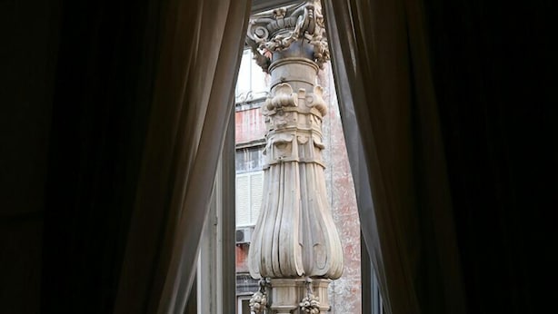 A view through a doorway with curtains, leading to an outdoor area with a large, ornate column and a metal railing. - Caravaggio Hotel (Naples)