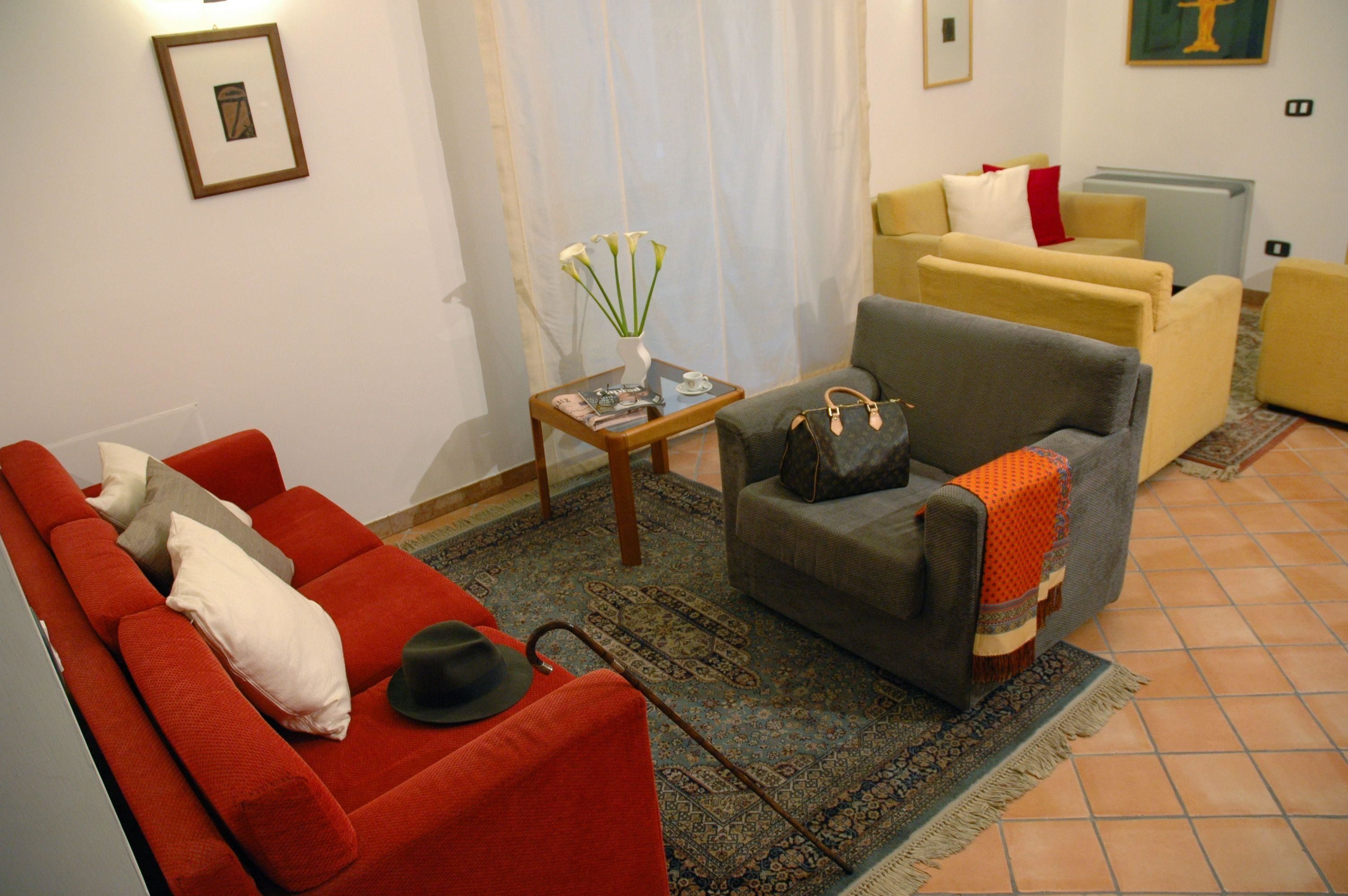 A living room with a red sofa, a grey armchair, and a yellow sofa. There is a small table with a vase of flowers and a magazine.