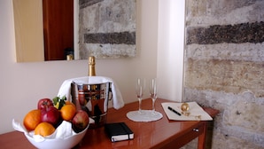 A wooden table with a fruit bowl, a bottle of champagne, two glasses, a notebook, and a pen. - Caravaggio Hotel (Naples)