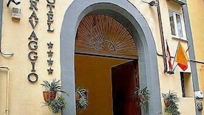 A hotel entrance with an arched doorway, potted plants, and a flag. - Caravaggio Hotel (Naples)