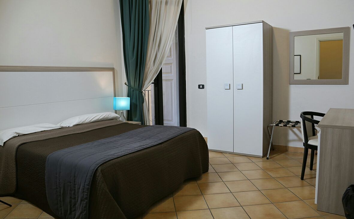 A hotel room with a bed, a wardrobe, a desk, and a chair.