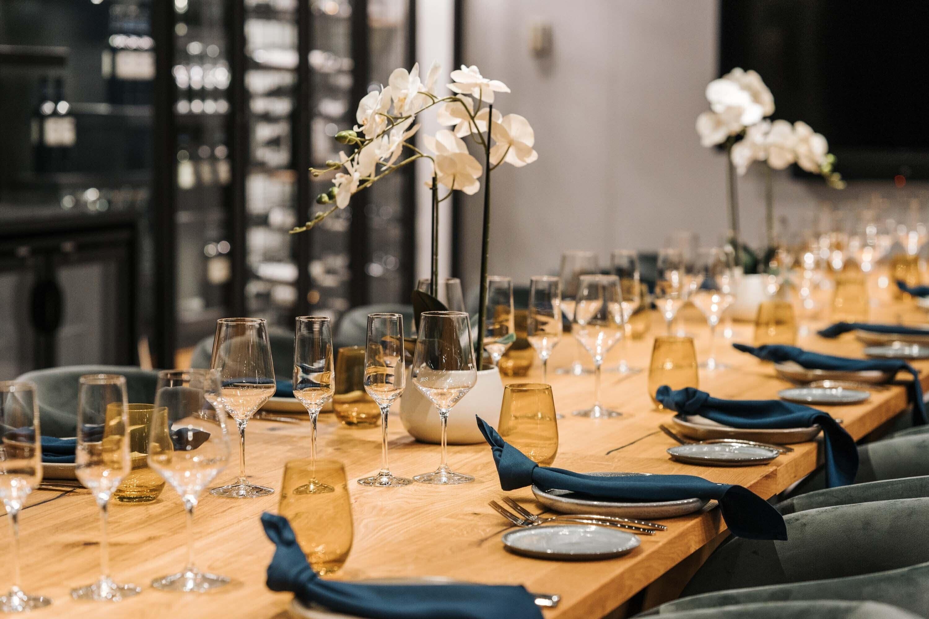 A long dining table set with multiple wine glasses, plates, and blue napkins.