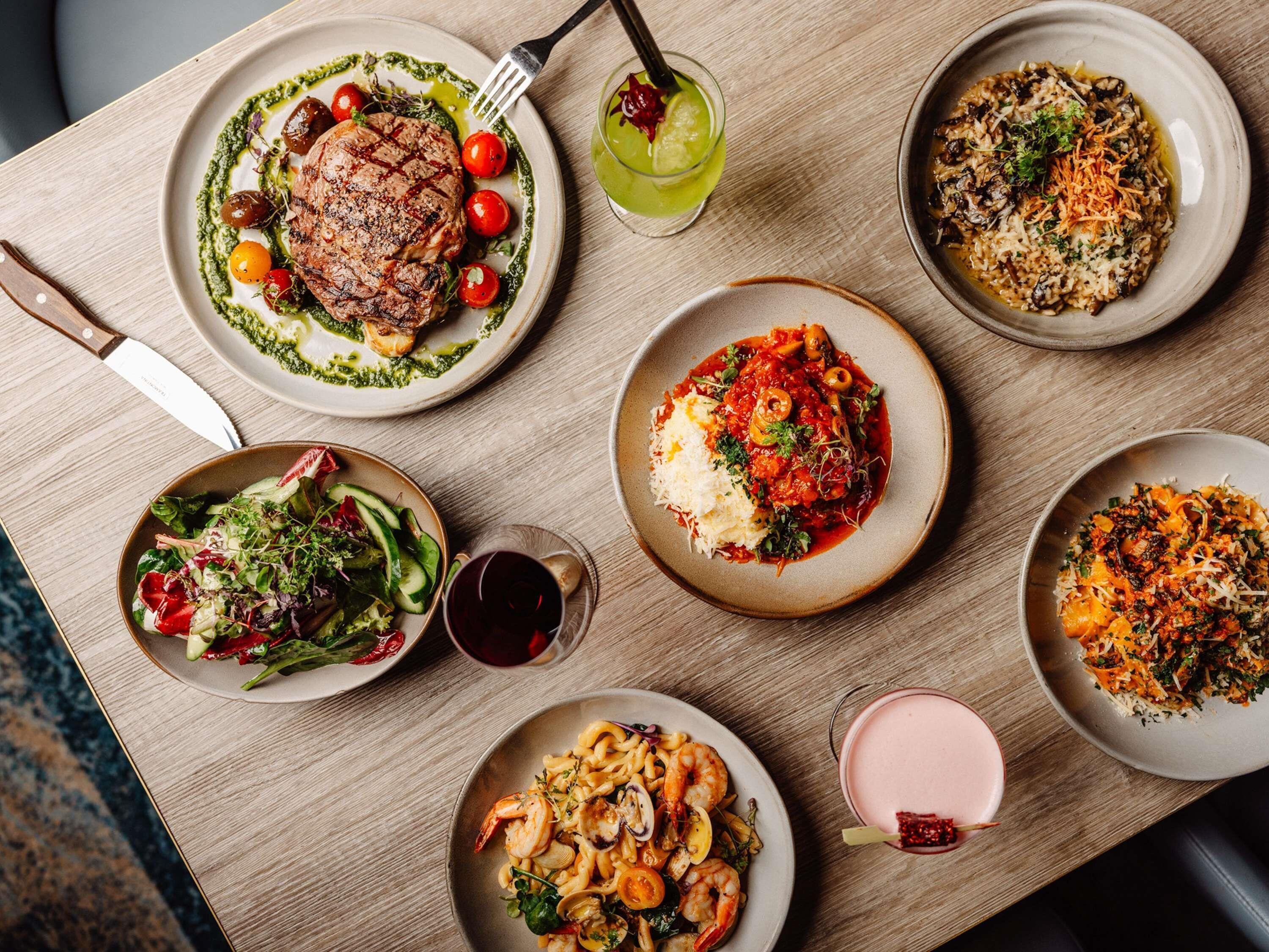 A table with various dishes, a knife, and a glass of red wine.
