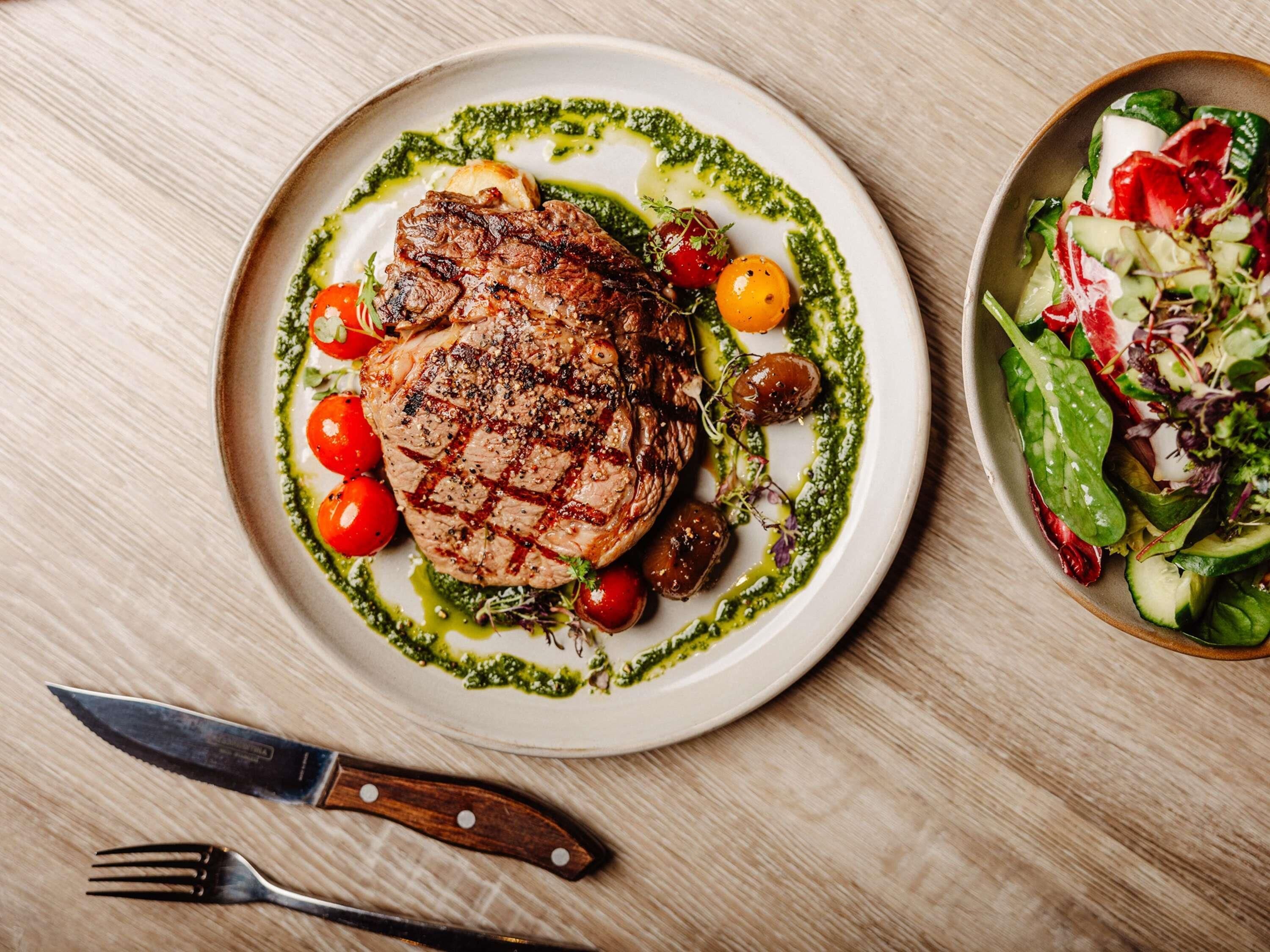 Une assiette de viande grillée accompagnée de légumes et d’une salade, le tout posé sur une table en bois.