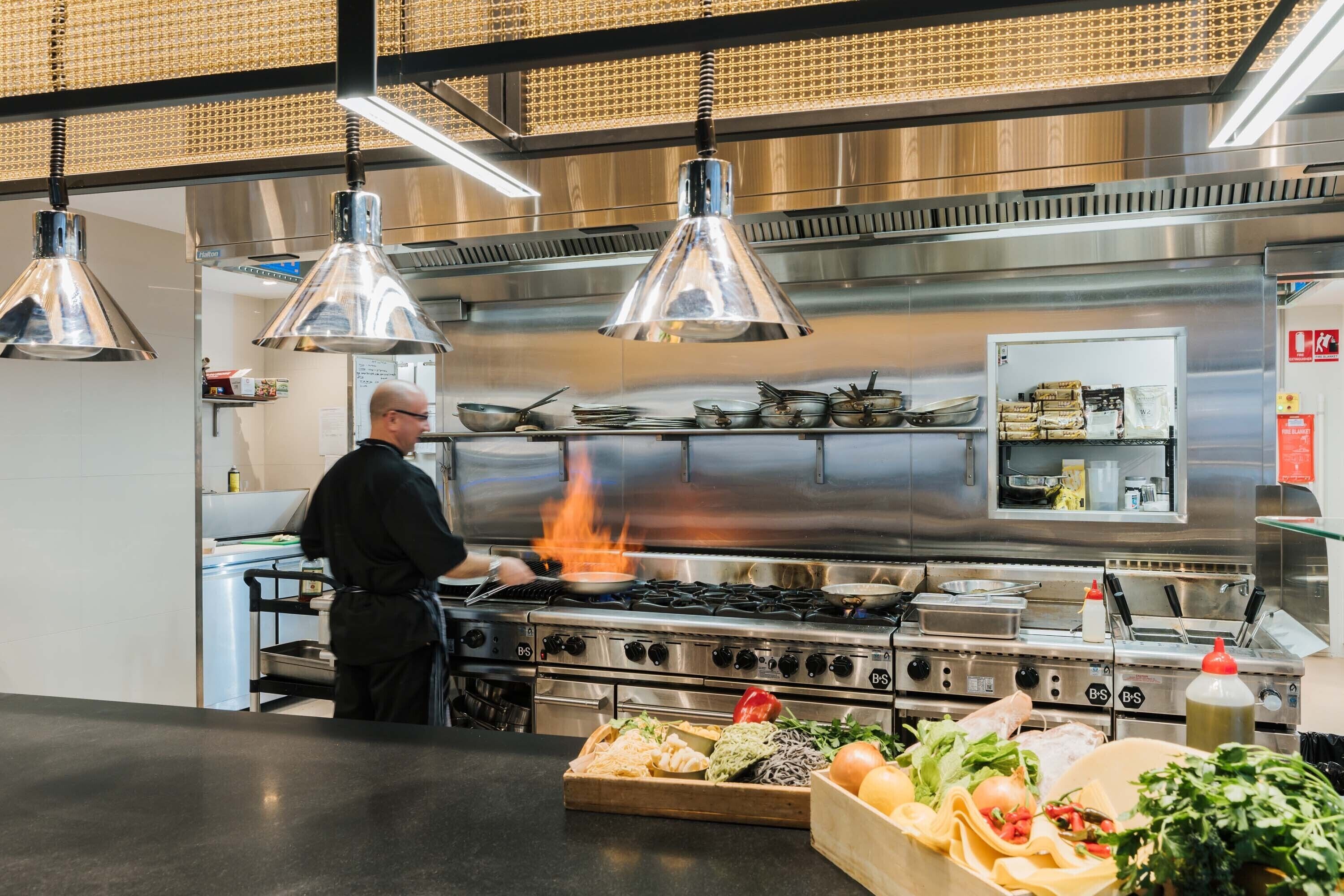 A modern kitchen with stainless steel appliances, hanging pendant lights, and a variety of fresh ingredients on the counter.