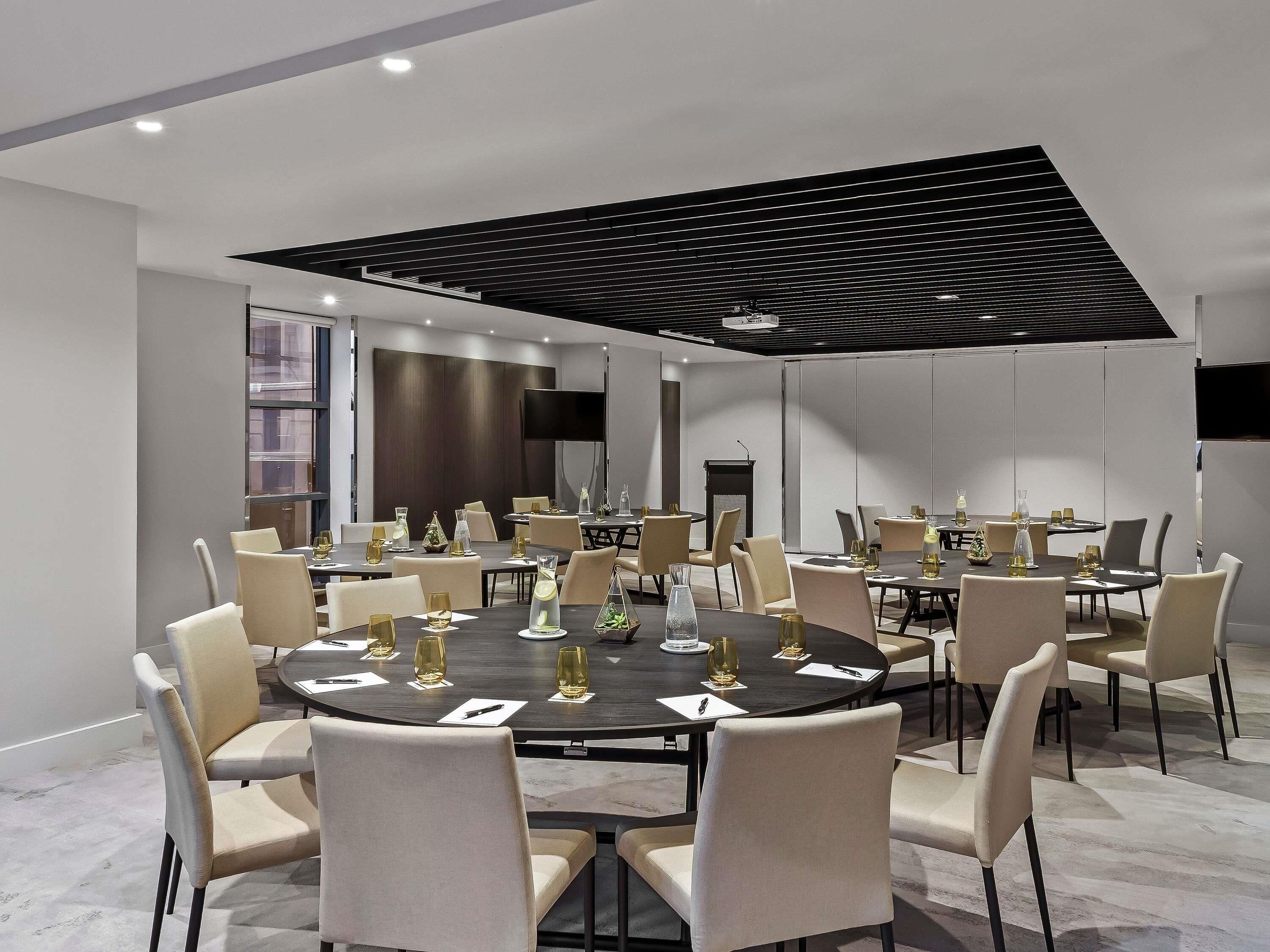 A modern conference room with round tables, beige chairs, and a large screen.