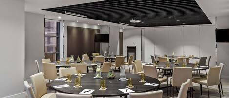 A modern conference room with round tables, beige chairs, and a large screen.
