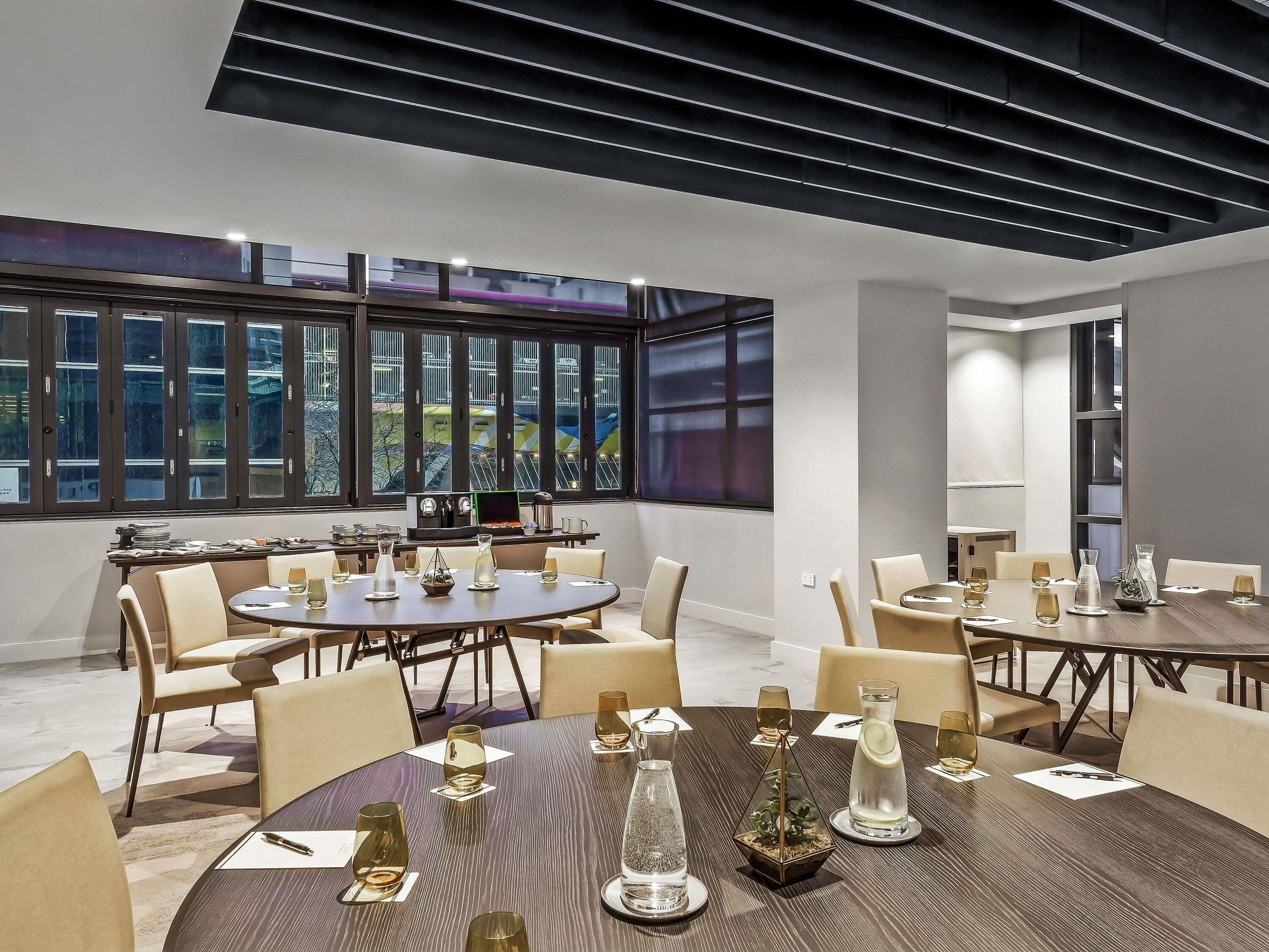 A modern dining area with round tables, chairs, and a large window with a city view.