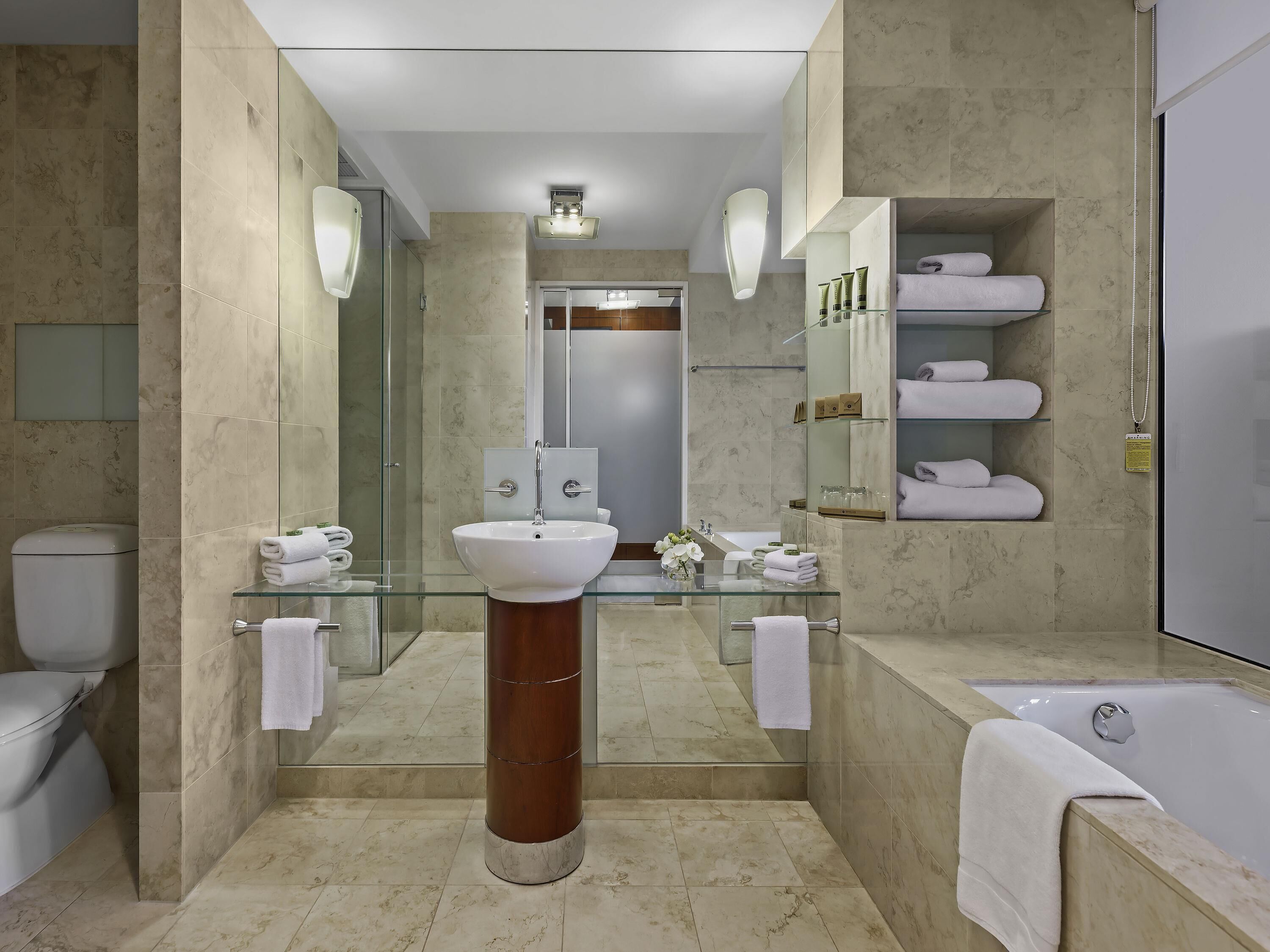 A modern bathroom with a glass sink, a large mirror, a bathtub, and marble flooring.