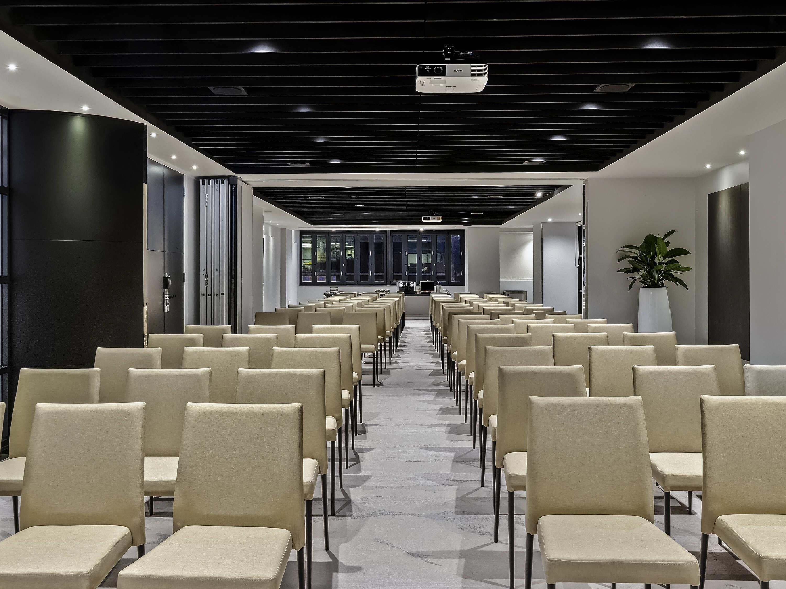 A conference room with rows of chairs, a projector, and a large potted plant.
