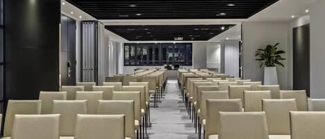 A conference room with rows of chairs, a projector, and a large potted plant.
